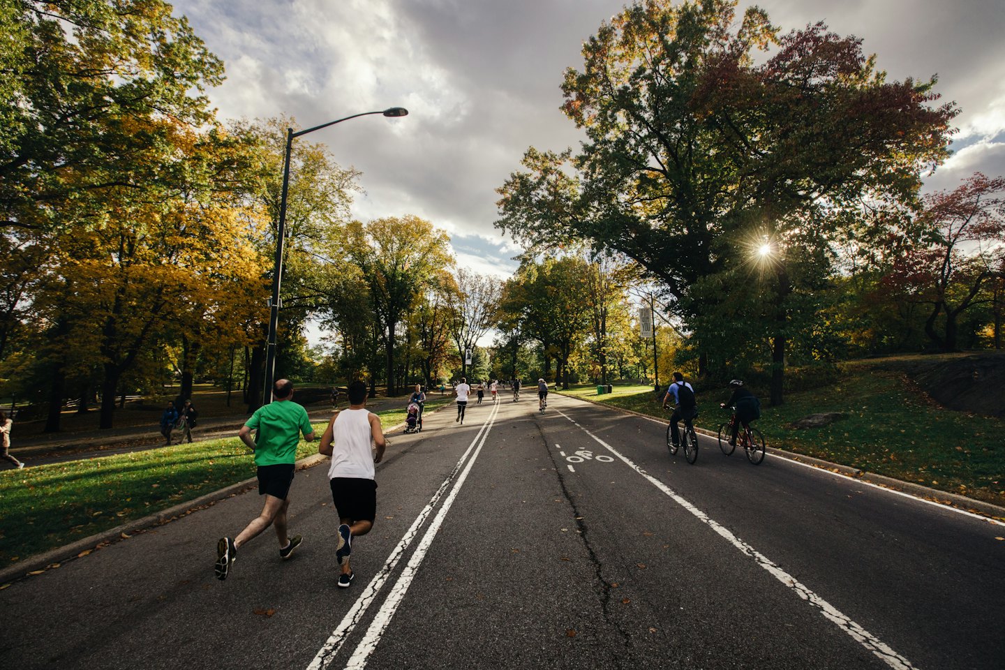 People jogging and cycling on a park path in autumn.