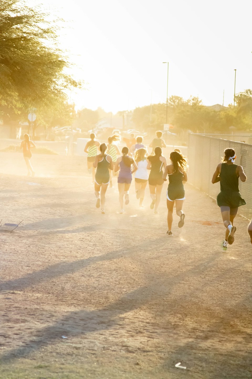 Young athletes run on a dusty path toward the sun.