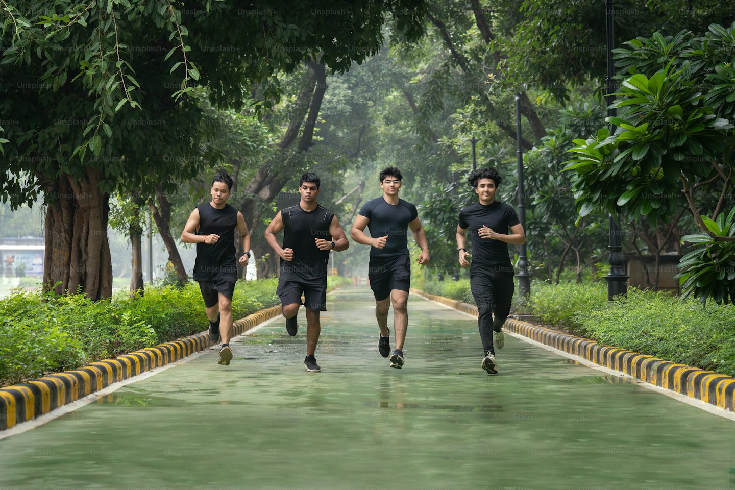Four men jog together on a paved park path.