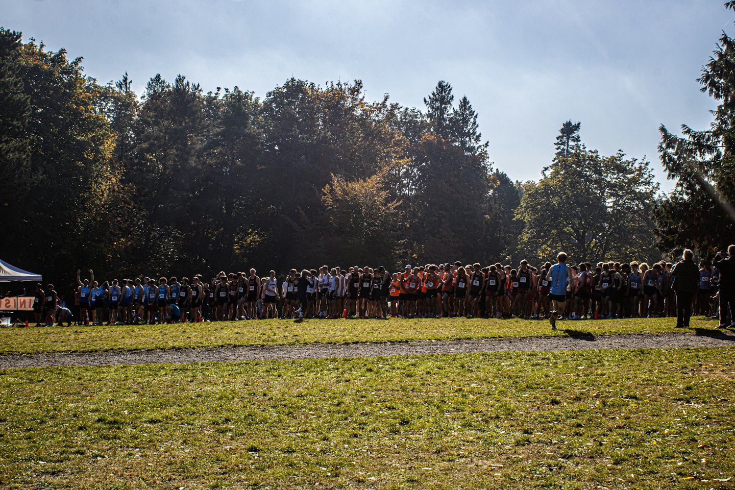 Teenage runners gathered shoulder-to-shoulder at a sunny cross country starting line.