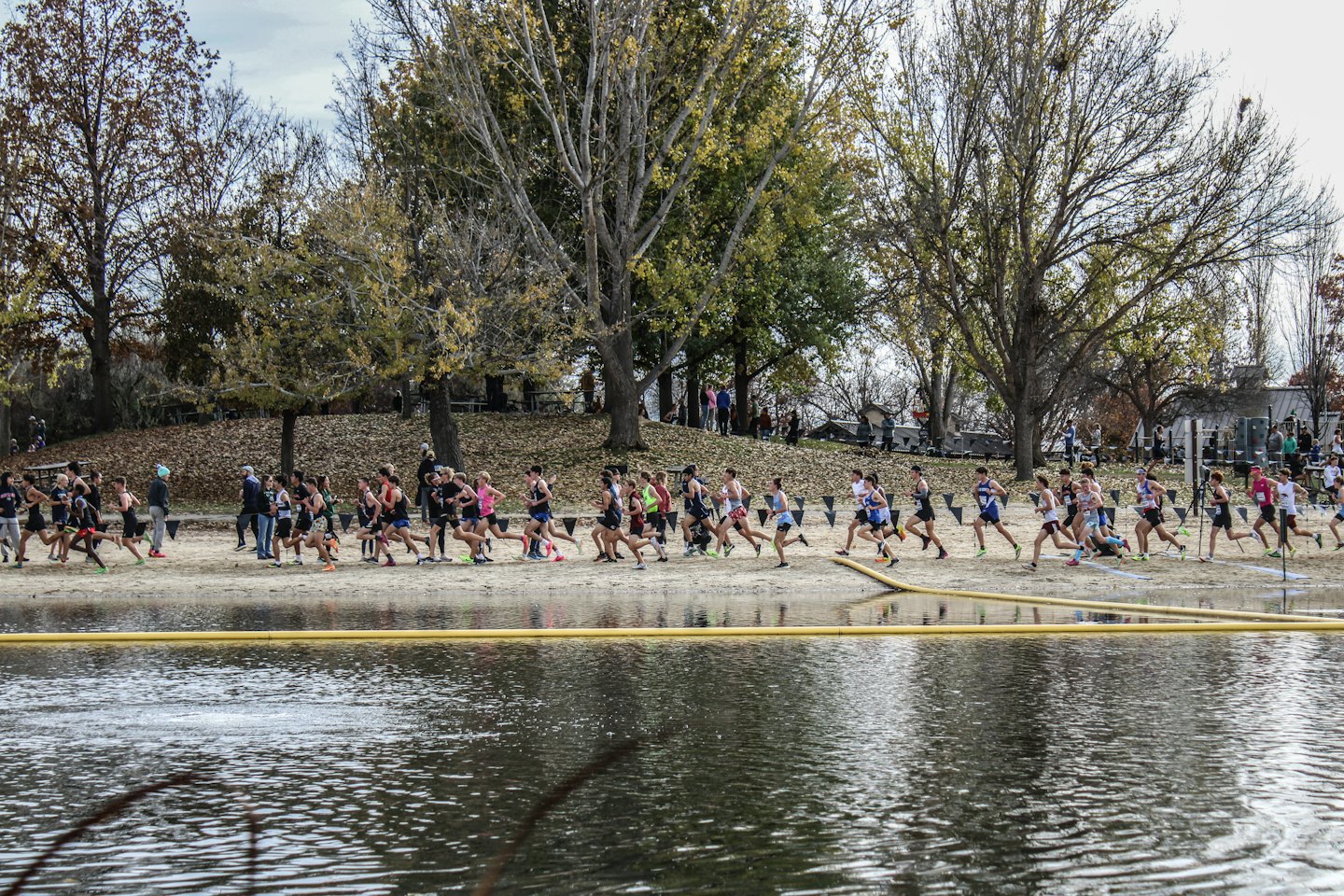 Diverse runners compete in a cross-country race by a lake.