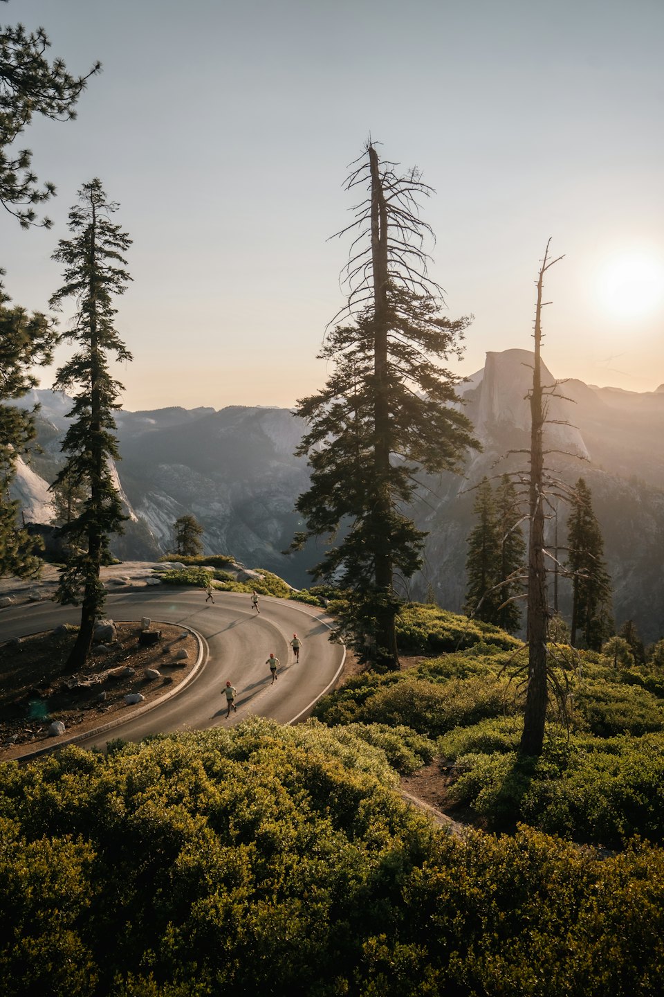 Runners on a winding road through mountains at golden hour.